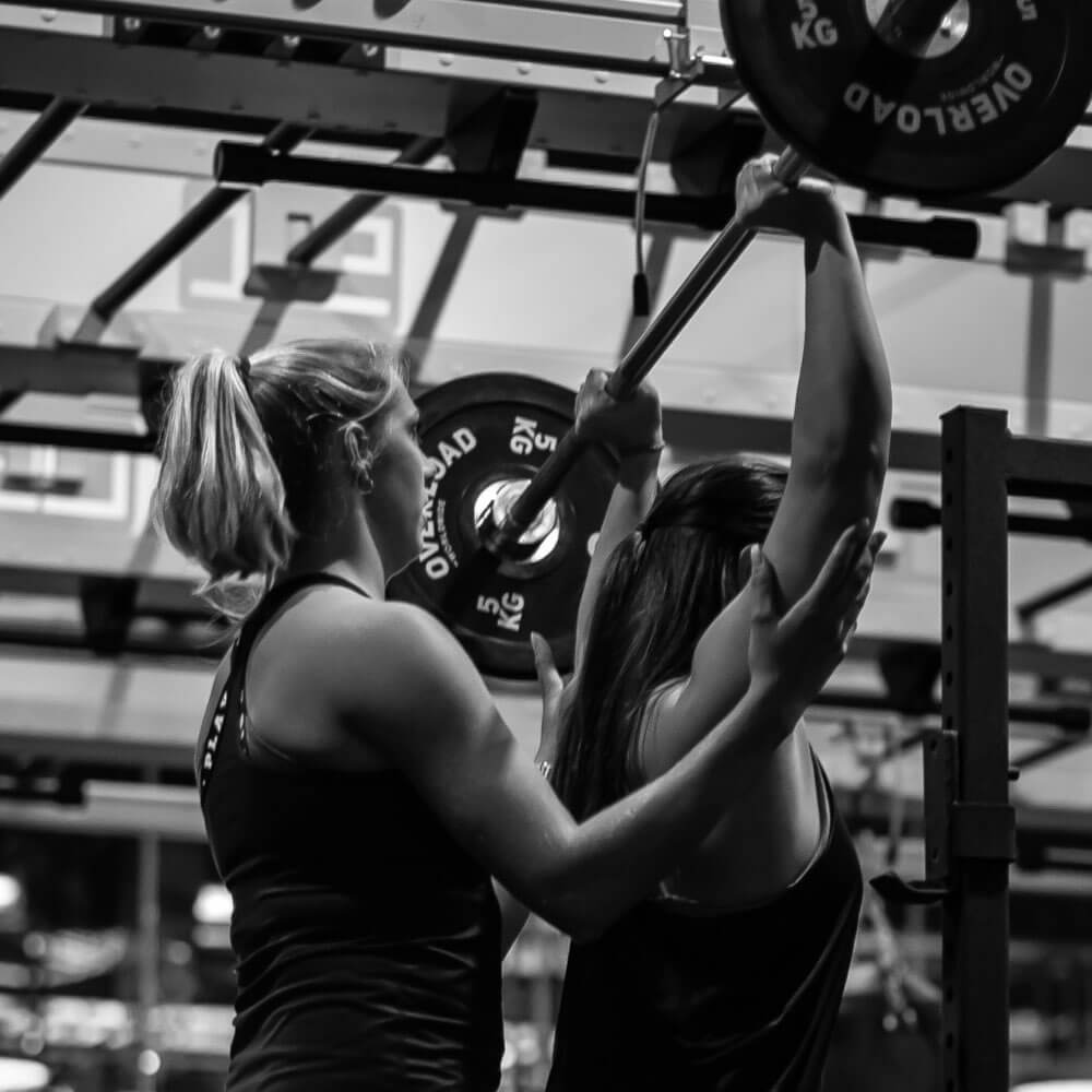 Two women lifting barbells in a gym.