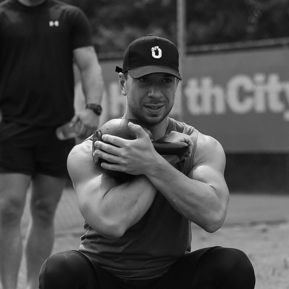 Black and white photo of a man squatting with a kettlebell.